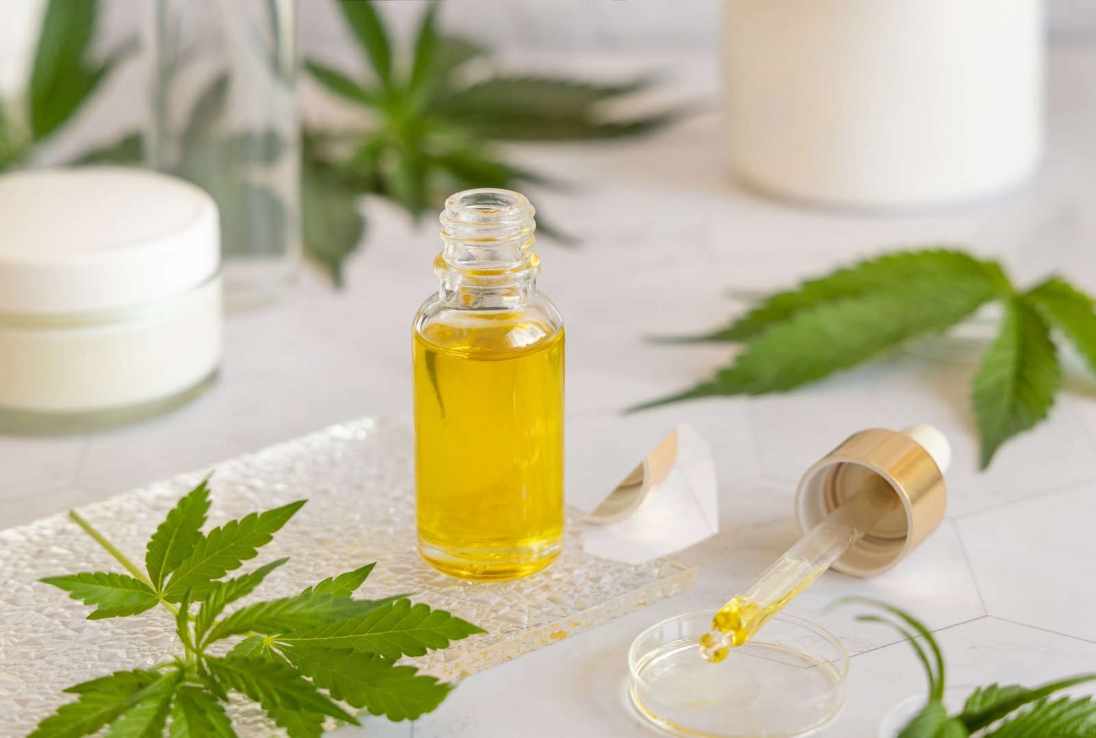 Opened Dropper bottle with pipette near green cannabis leaves. CBD oil